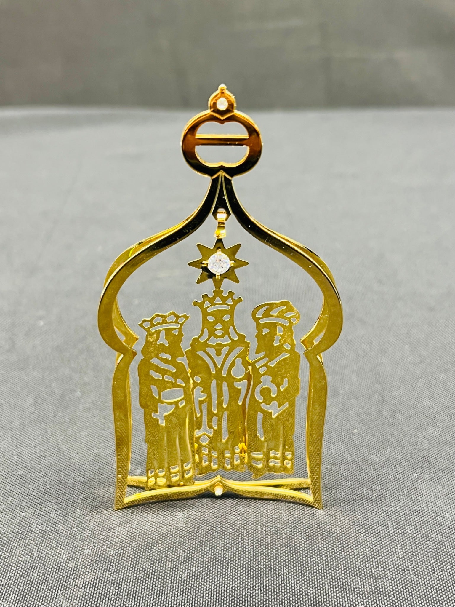 Gold decorative item with three figures and a star on a gray background