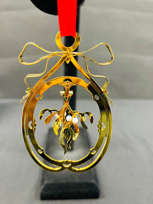 Gold Christmas ornament with mistletoe design on a red ribbon against a gray background