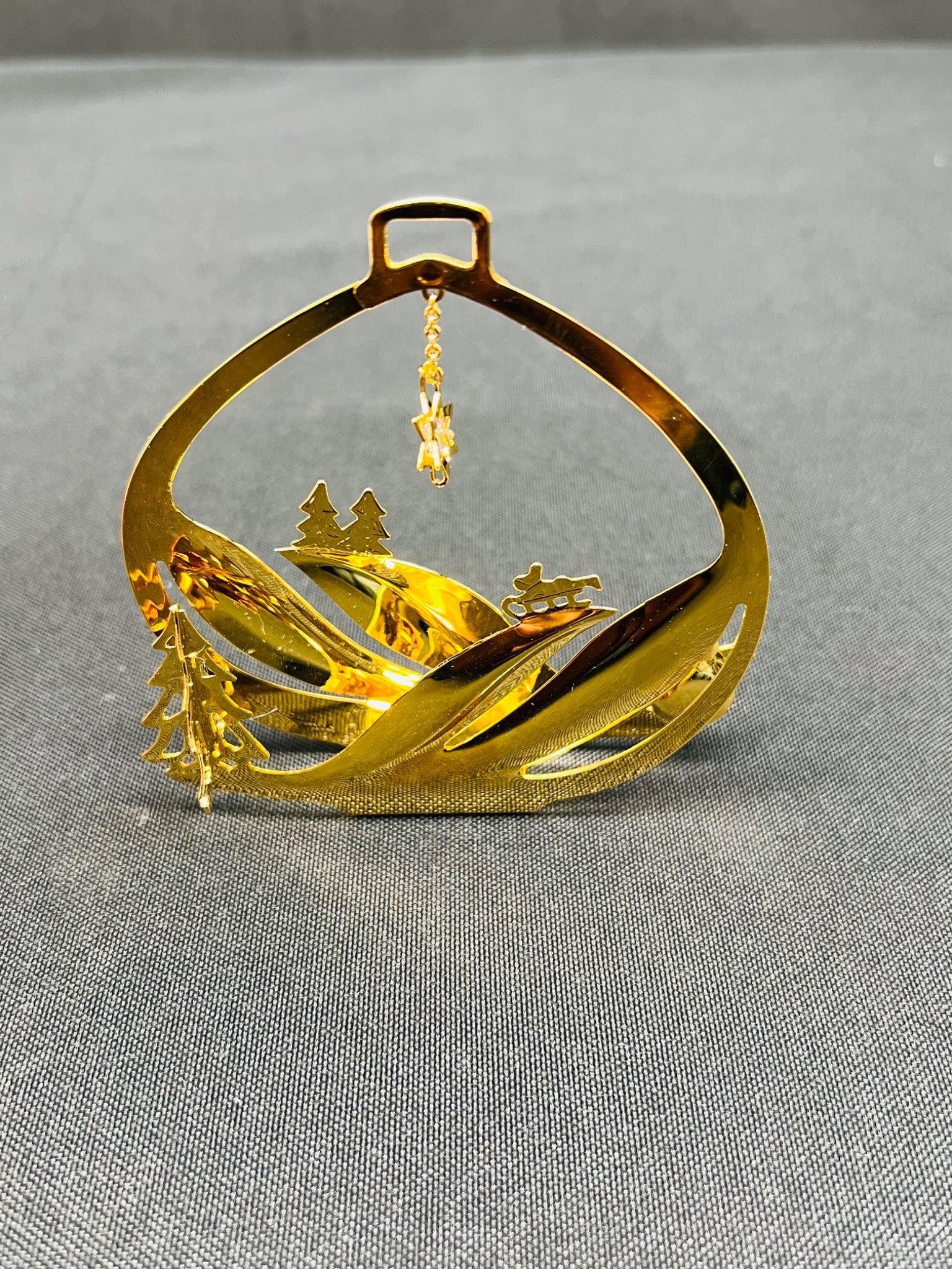 Gold ornament with mountain and tree design on a gray background