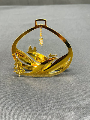 Gold ornament with mountain and tree design on a gray background