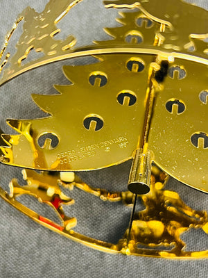 Gold metal decorative item with intricate designs on a gray background