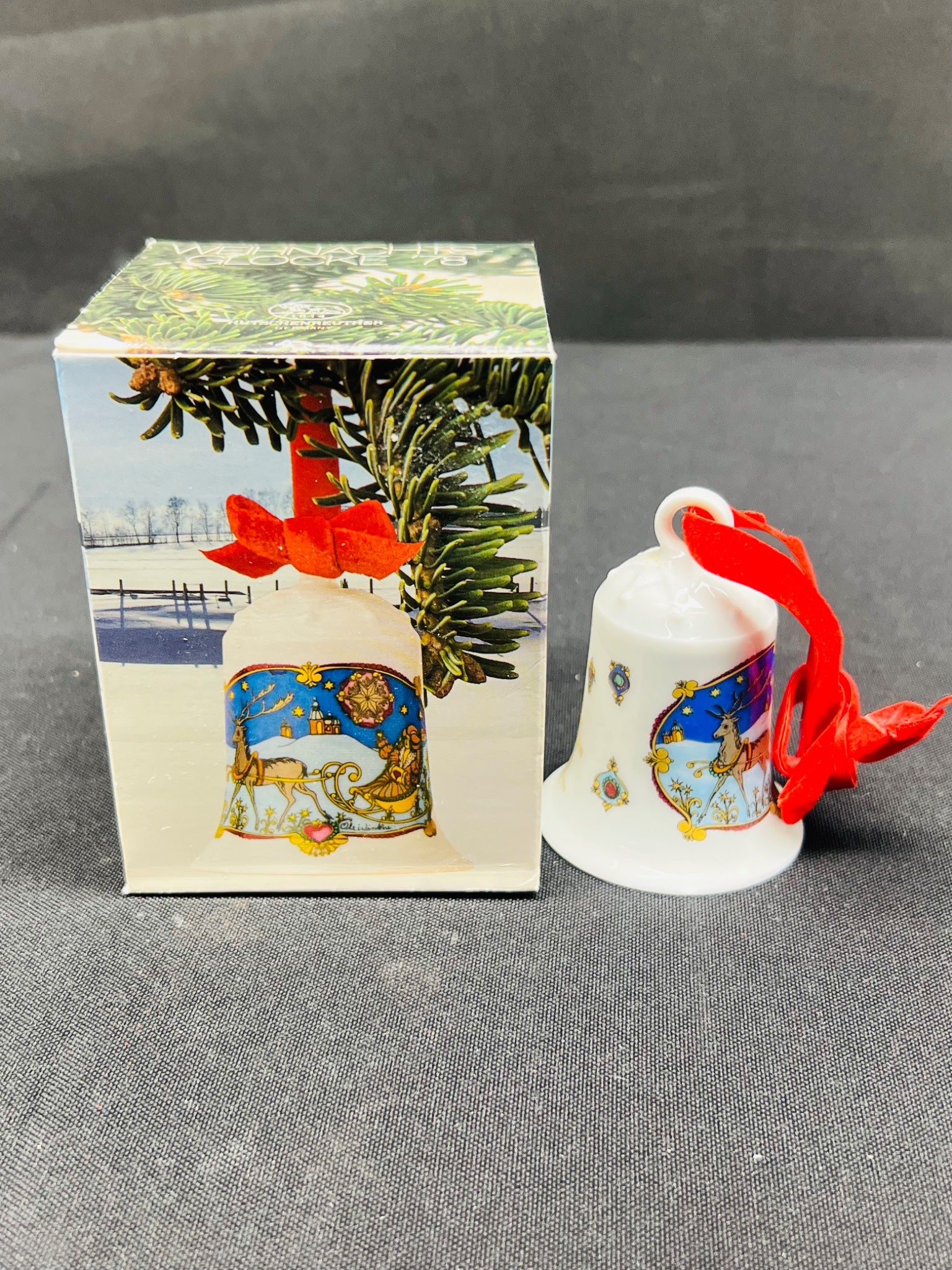 Decorative bell with red ribbon next to its packaging on a gray surface