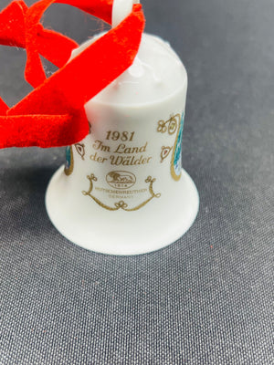 White bell-shaped object with gold text and a red decorative bow on a gray background