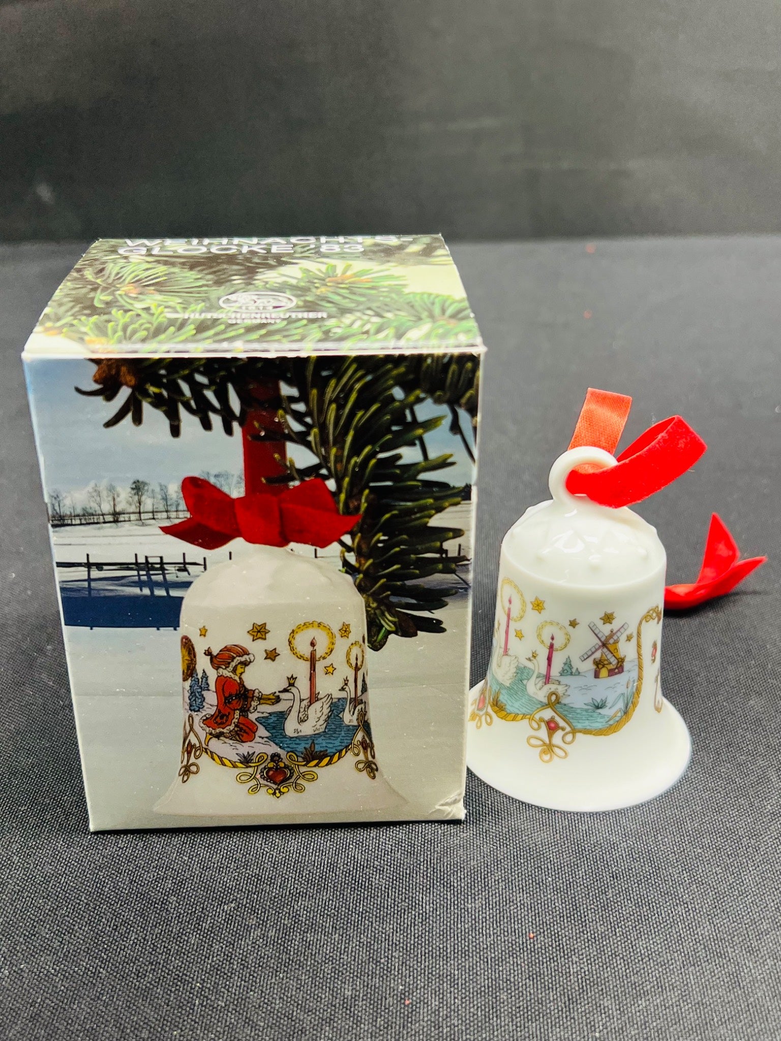 Decorative bell with festive design next to its packaging on a gray surface