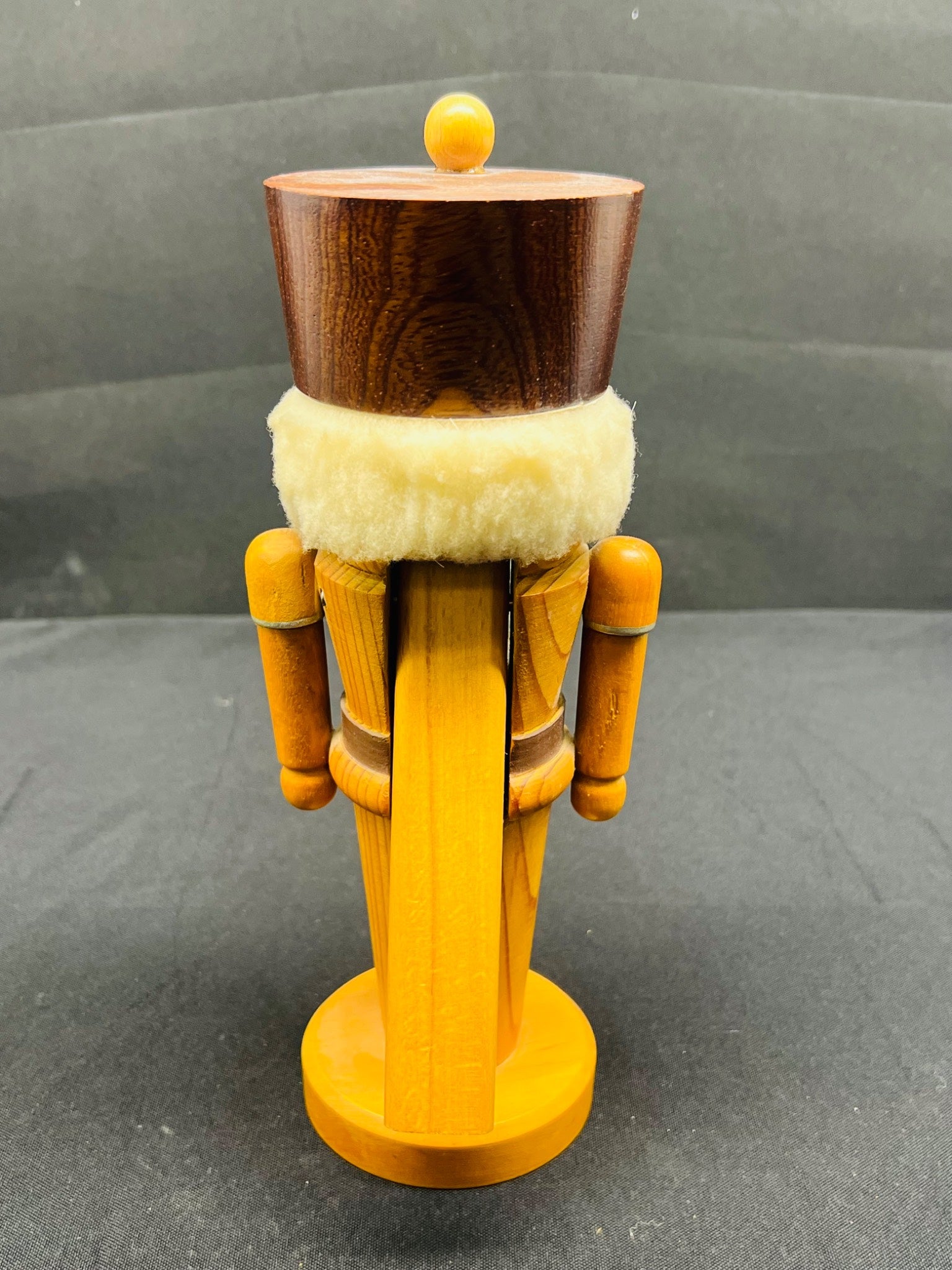 Wooden nutcracker figurine with a dark brown top and yellow body on a gray background