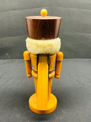 Wooden nutcracker figurine with a dark brown top and yellow body on a gray background