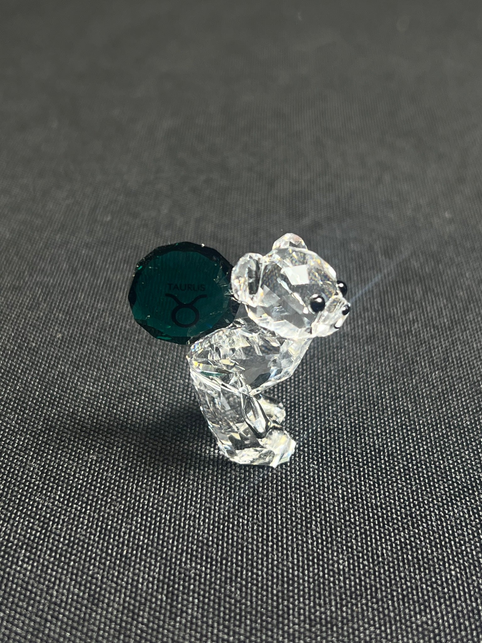 Crystal bear figurine with green gemstone on a gray background