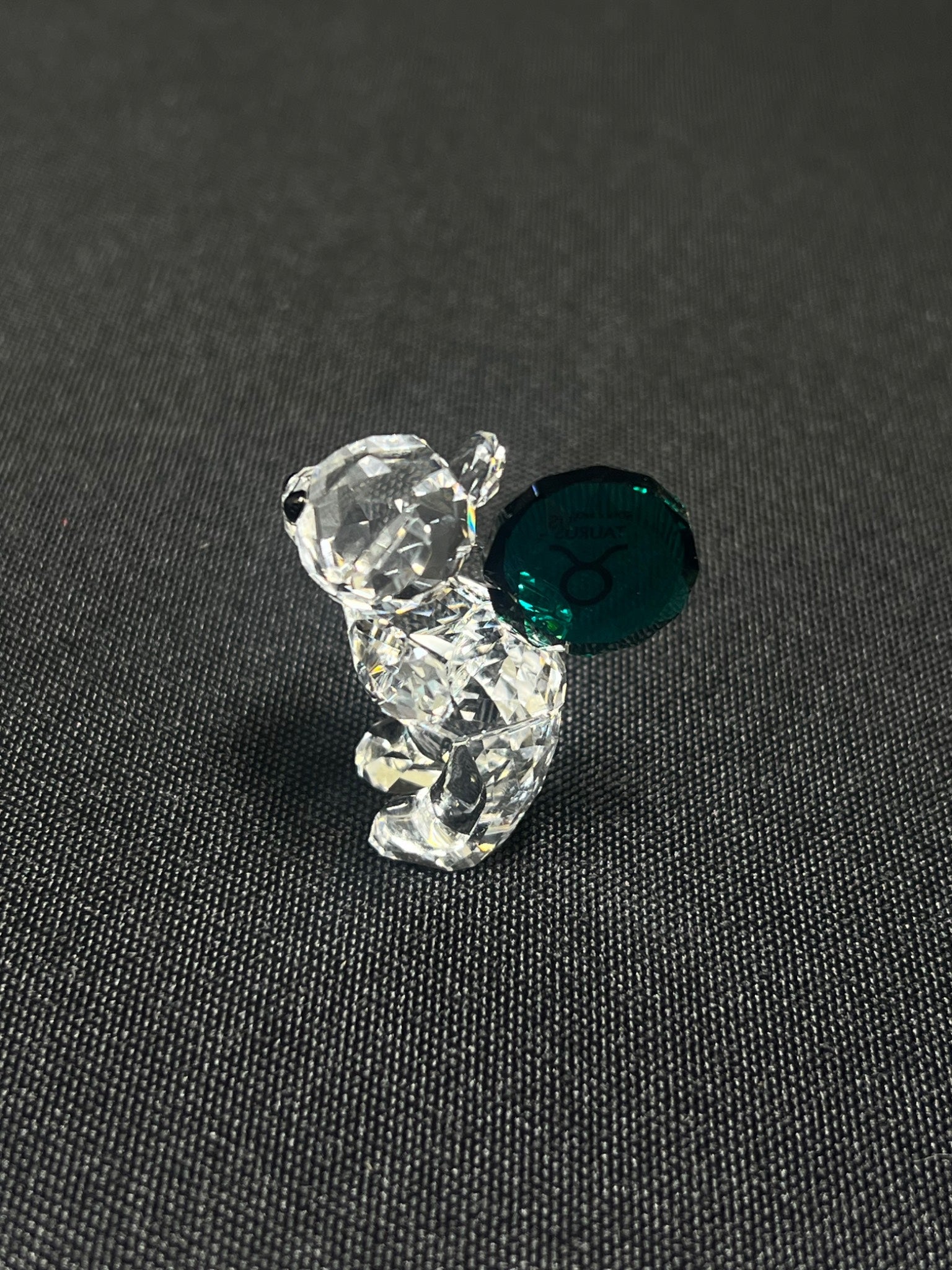 Crystal bear figurine with a green gem on a dark textured surface