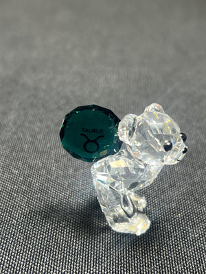Crystal bear figurine with a green gemstone on a gray background