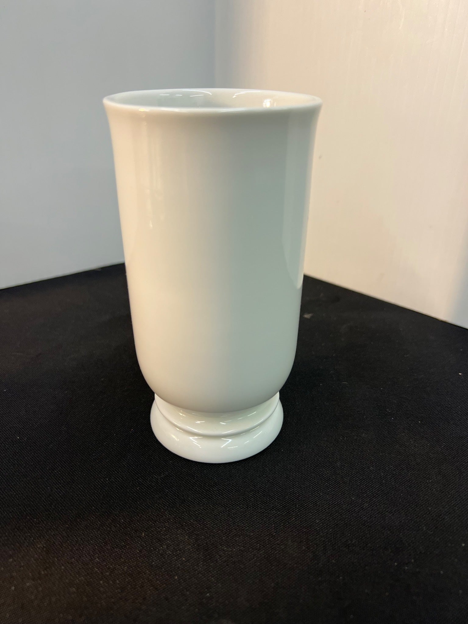 White ceramic vase on a black surface with a plain background