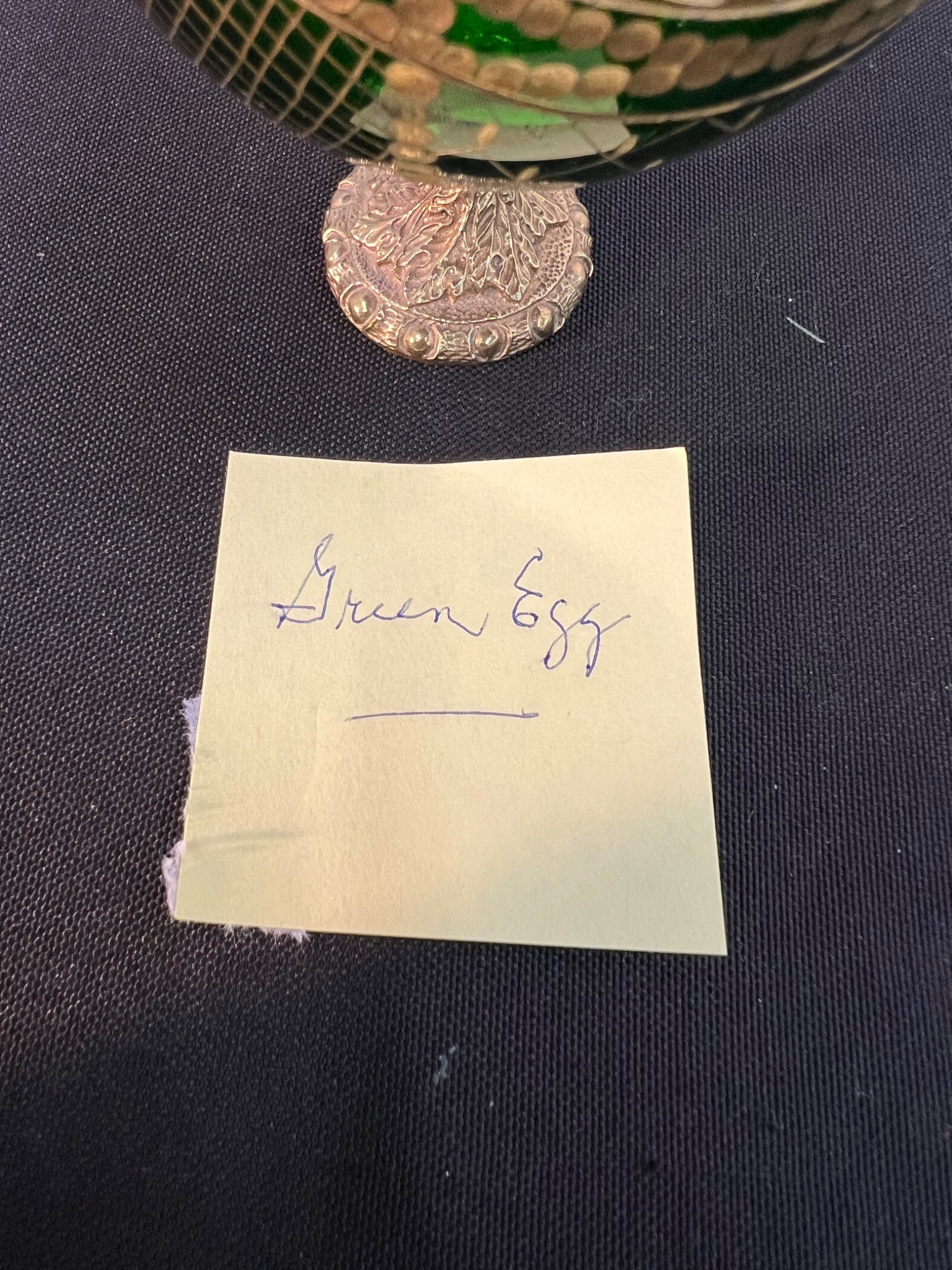 Small green object with a silver coin on a dark surface, labeled 'Green Egg'.