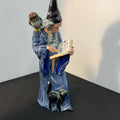 Decorative figurine of a wizard with a book and cats on a dark surface.