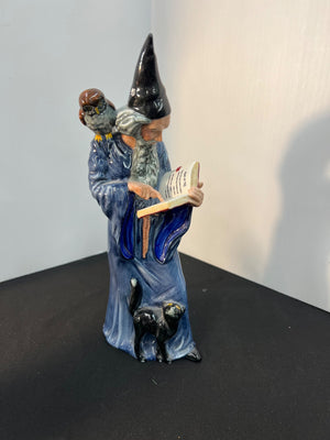 Decorative figurine of a wizard with a book and cats on a dark surface.
