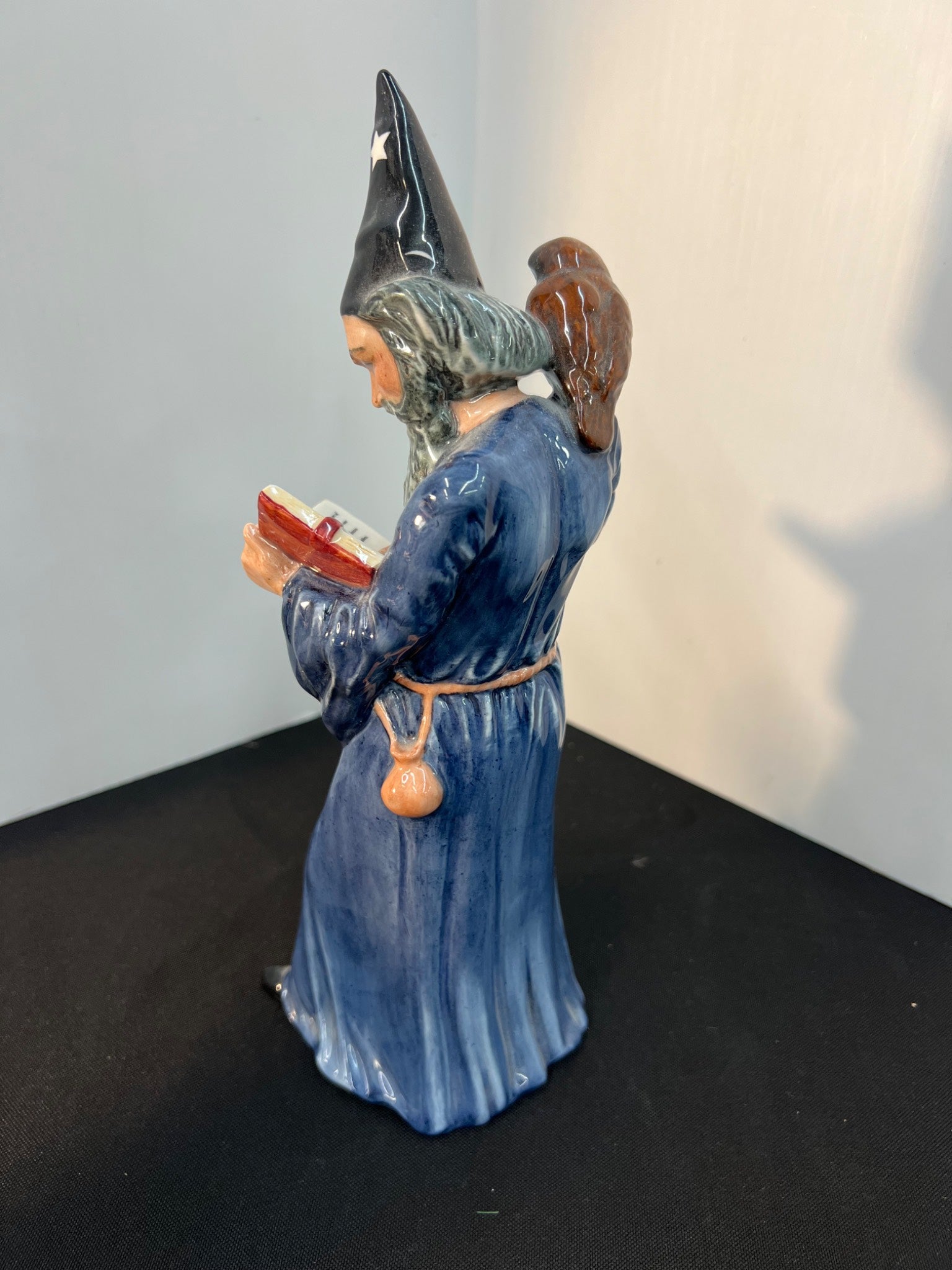 Statue of a wizard in blue robe holding a book against a plain background