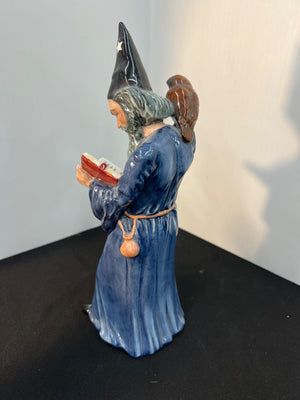 Statue of a wizard in blue robe holding a book against a plain background