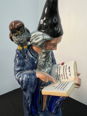 Decorative figurine of a man with a bird on his shoulder reading a book against a plain background
