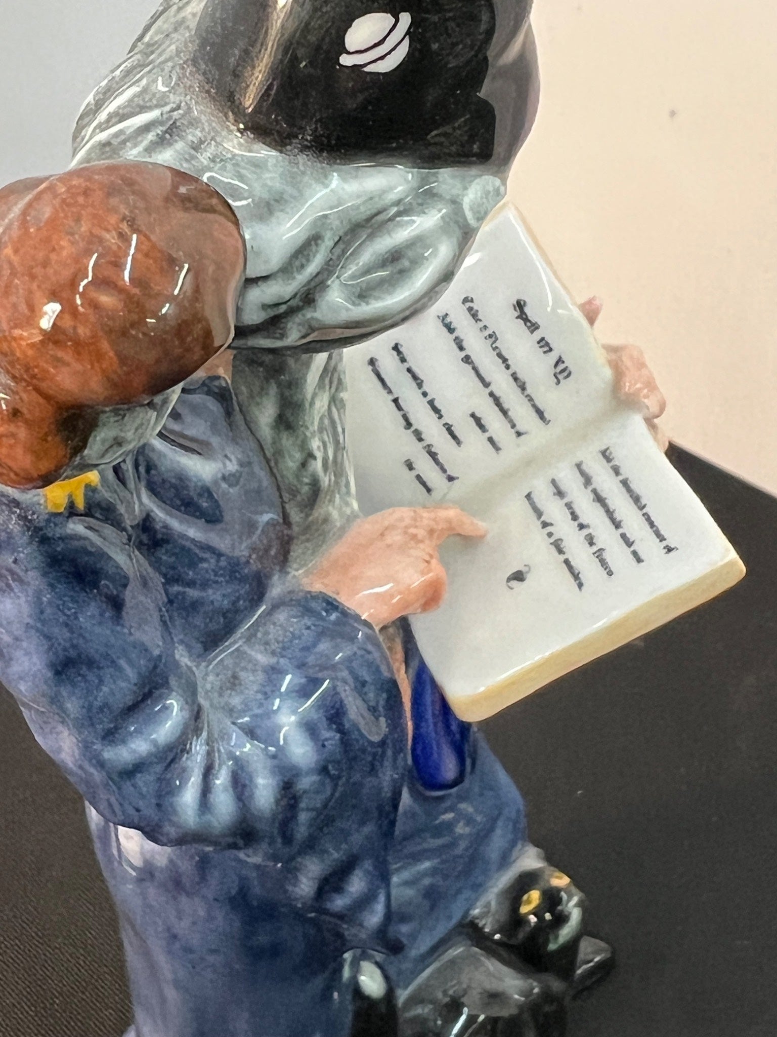 Statue of a person in a blue uniform holding a book with text, on a plain background.