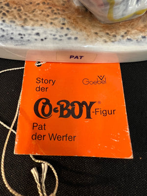 Orange tag with text about a Goebel Co-Boy figurine on a textured surface