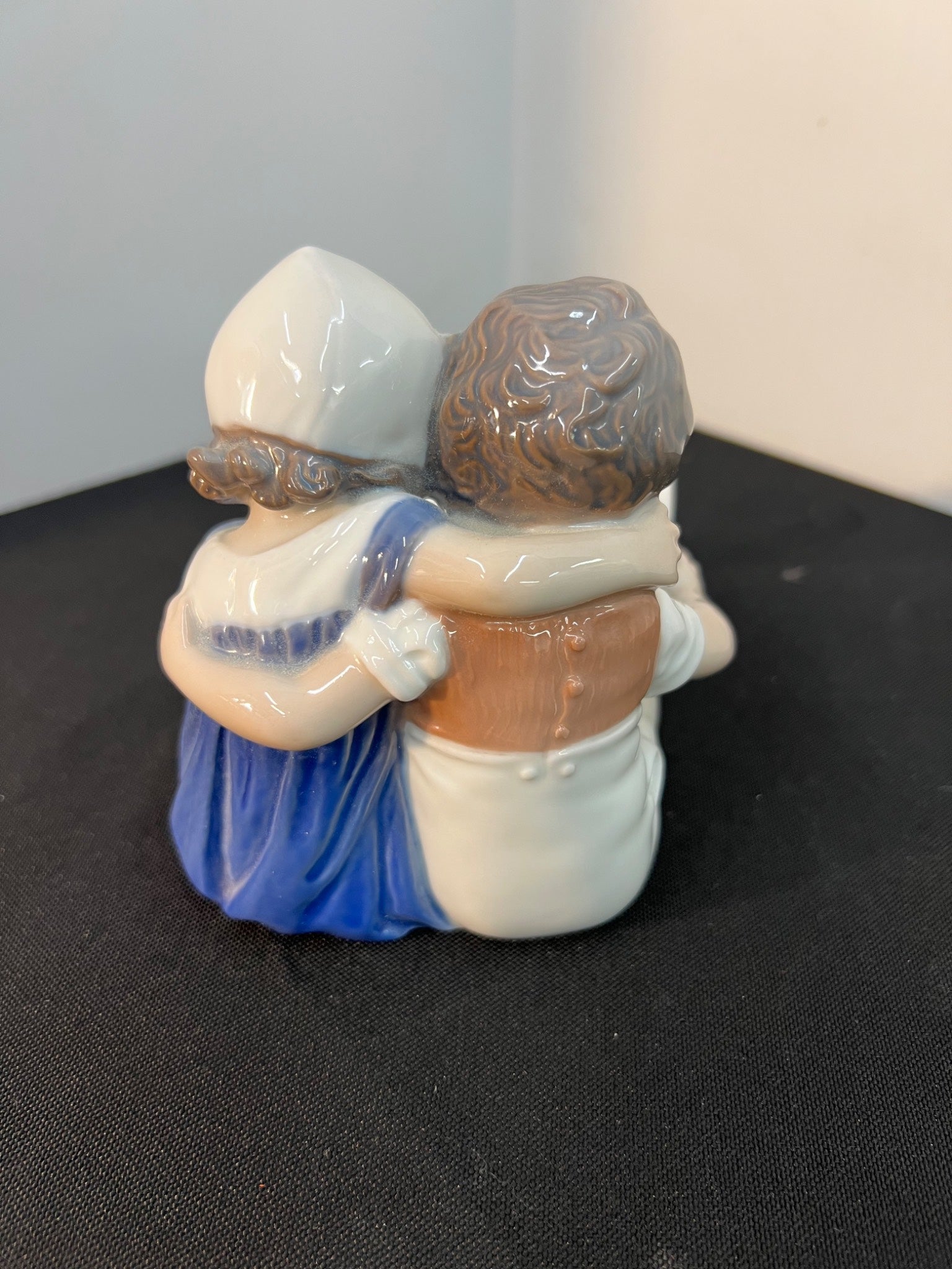 Two figurines hugging on a black surface with a gray background