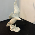 White ceramic sculpture of a bird on a black surface with a light gray background