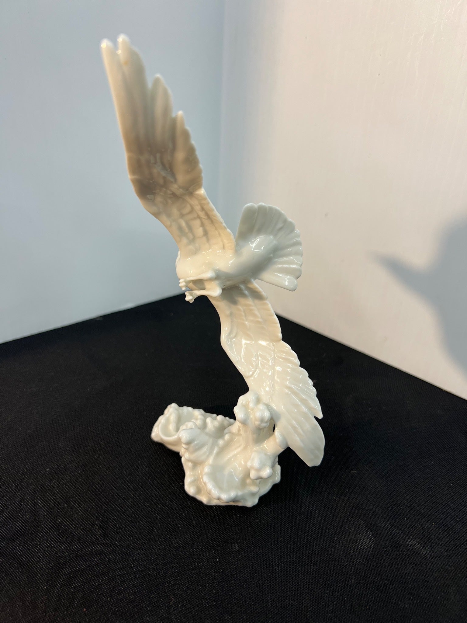 White ceramic sculpture of a bird in flight on a black surface with a light gray background