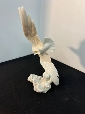 White ceramic sculpture of a bird in flight on a black surface with a light gray background