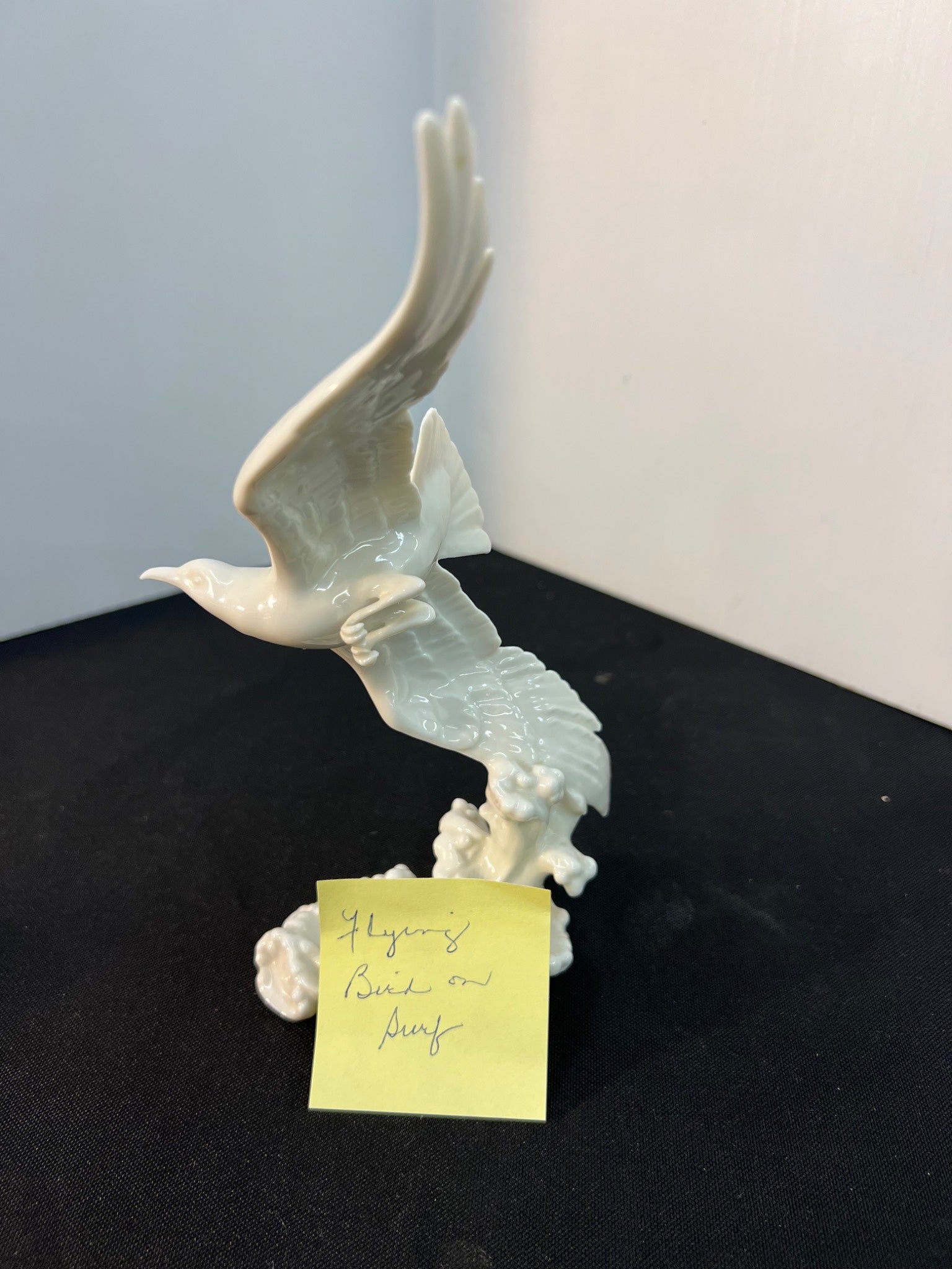 Decorative sculpture of a bird on a stand with a label on a black surface.