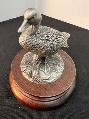 Bronze duck sculpture on a wooden base against a black background