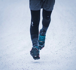 Person wearing black leggings and blue running shoes walking on a snowy ground.