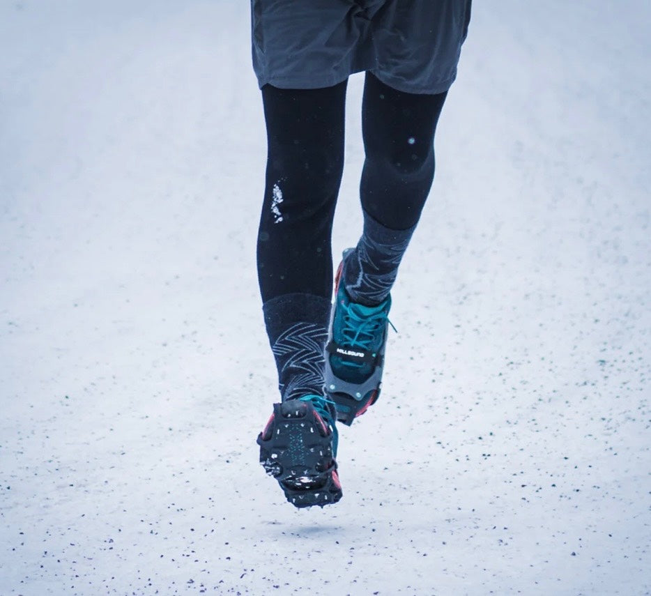 Person wearing black leggings and blue running shoes walking on a snowy ground.