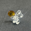 Clear glass bear figurine with a yellow gemstone on a gray background