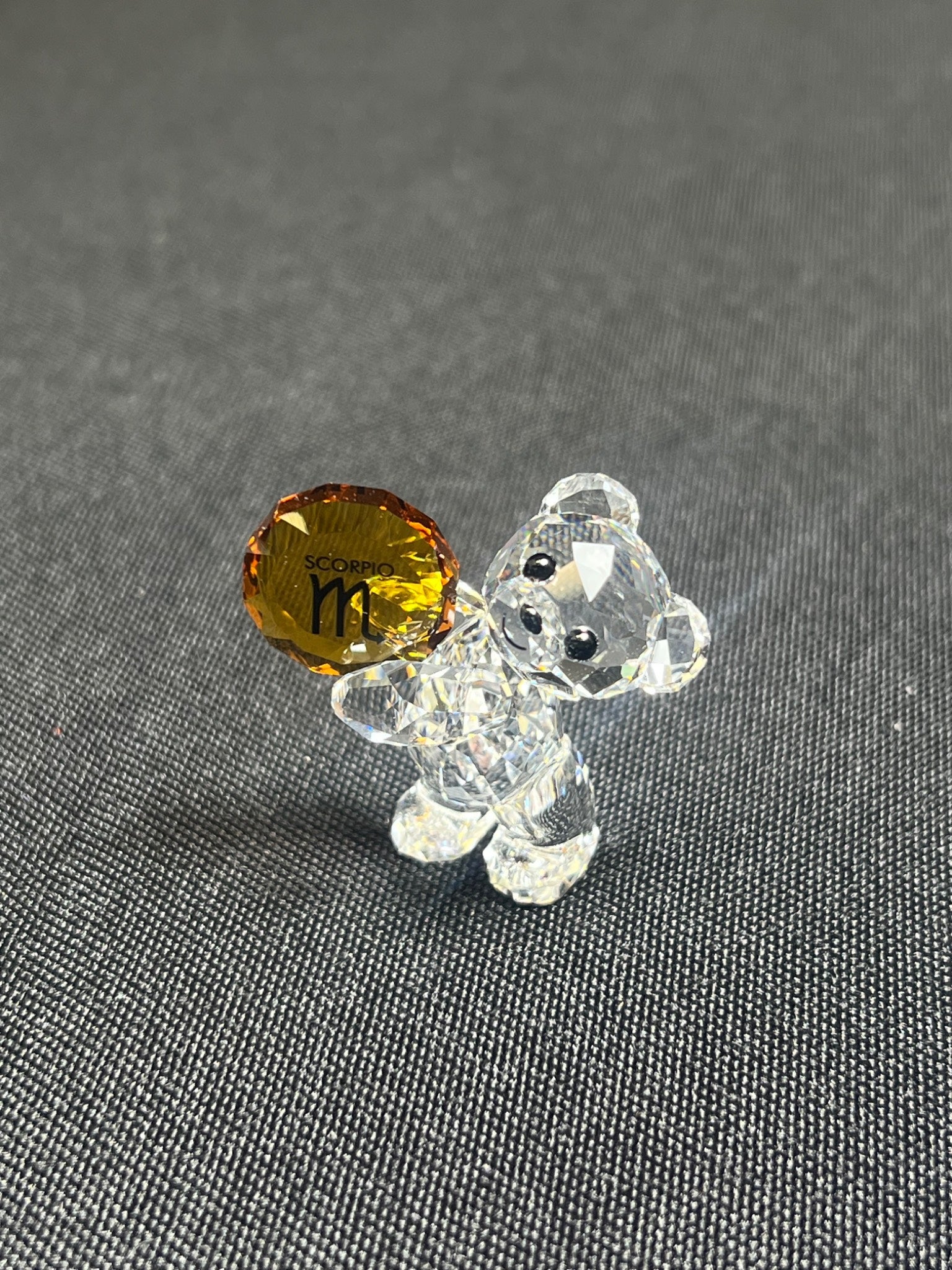 Clear glass bear figurine with a yellow gemstone on a gray background