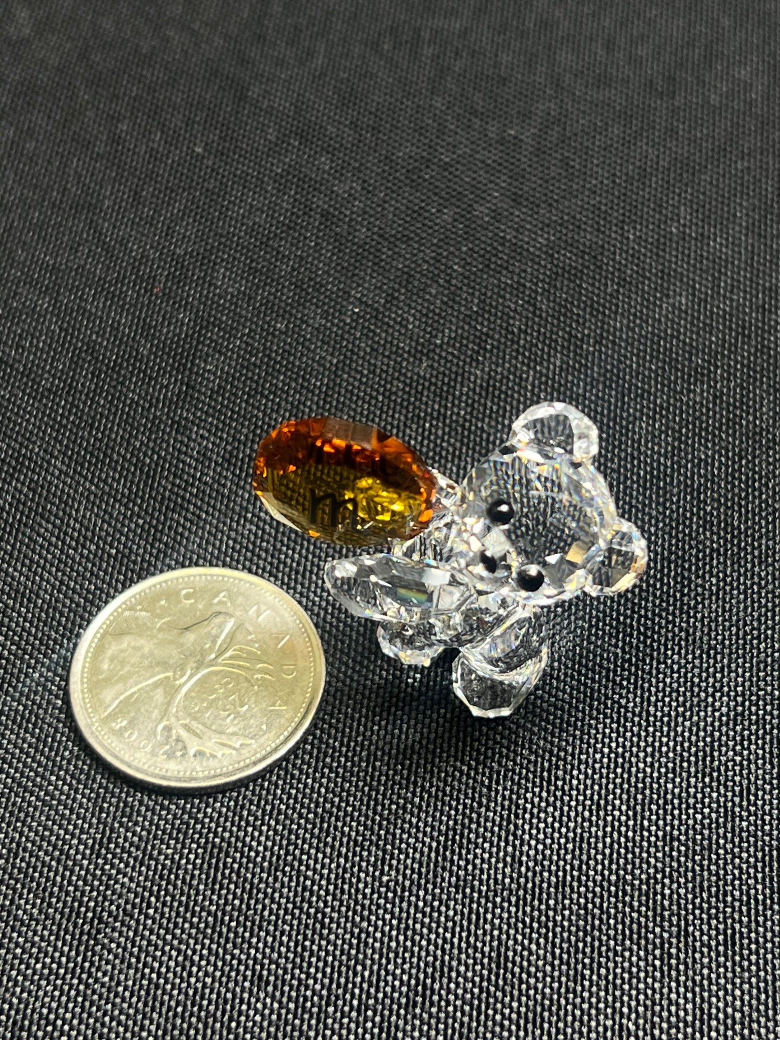 Small crystal bear figurine with a brown gemstone next to a coin on a black background