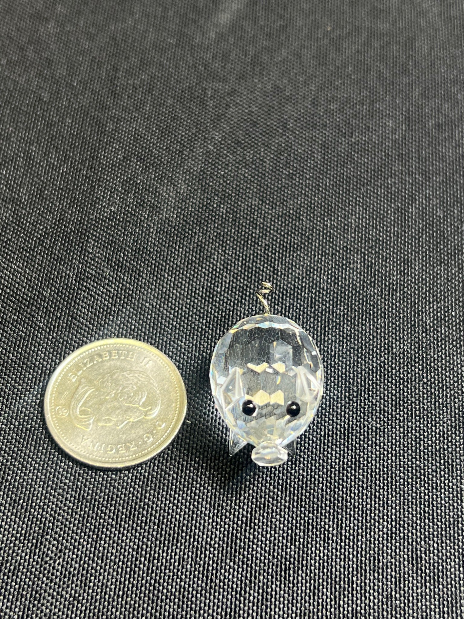 Small glass hedgehog figurine next to a coin on a dark fabric background