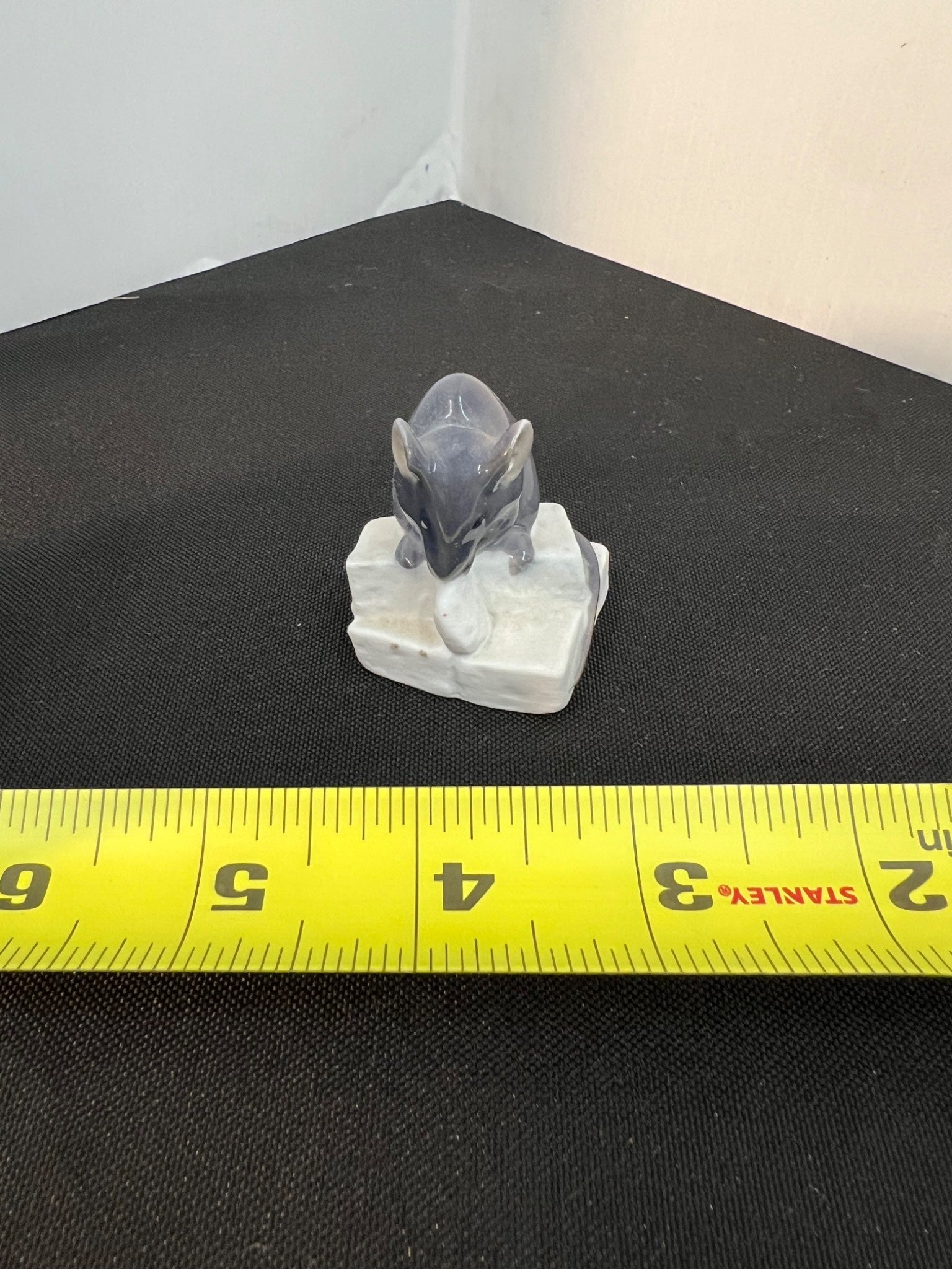 Small figurine of a mouse on a white base with a yellow measuring tape for scale.