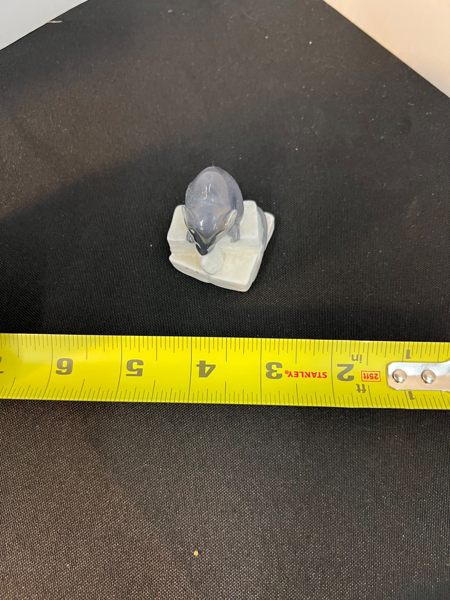 Small figurine on a black surface with a yellow measuring tape for scale.