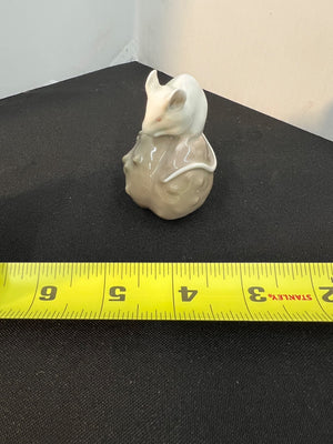 Small ceramic mouse figurine on a black surface with a measuring tape for scale.