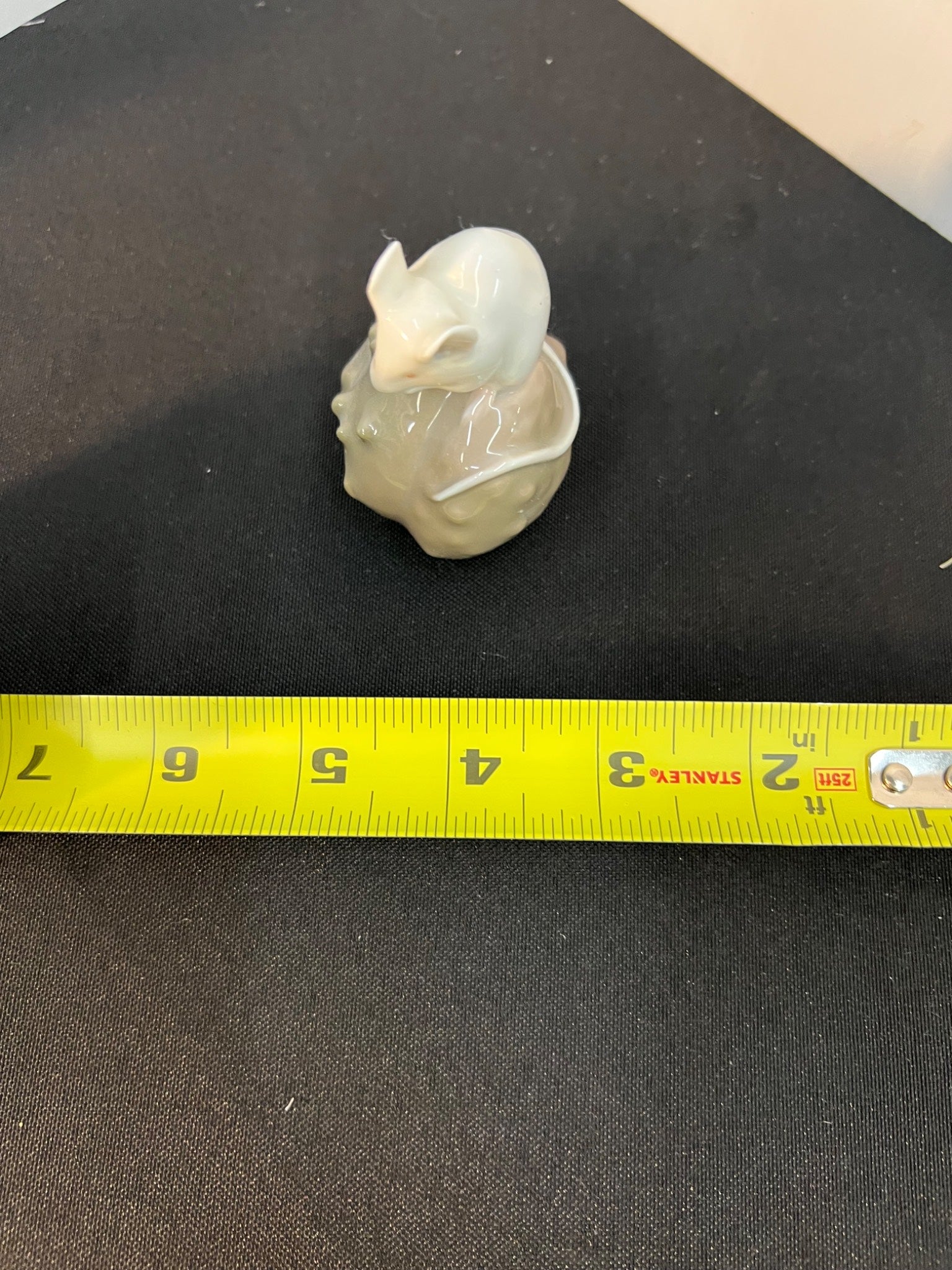 Small ceramic mouse figurine on a black surface with a measuring tape for scale.
