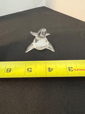 Small glass figurine of a penguin on a black surface with a yellow measuring tape for scale.