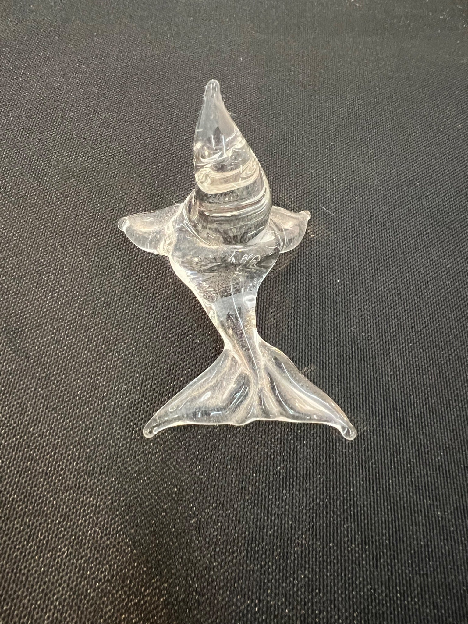 Glass sculpture of a fish on a dark fabric background