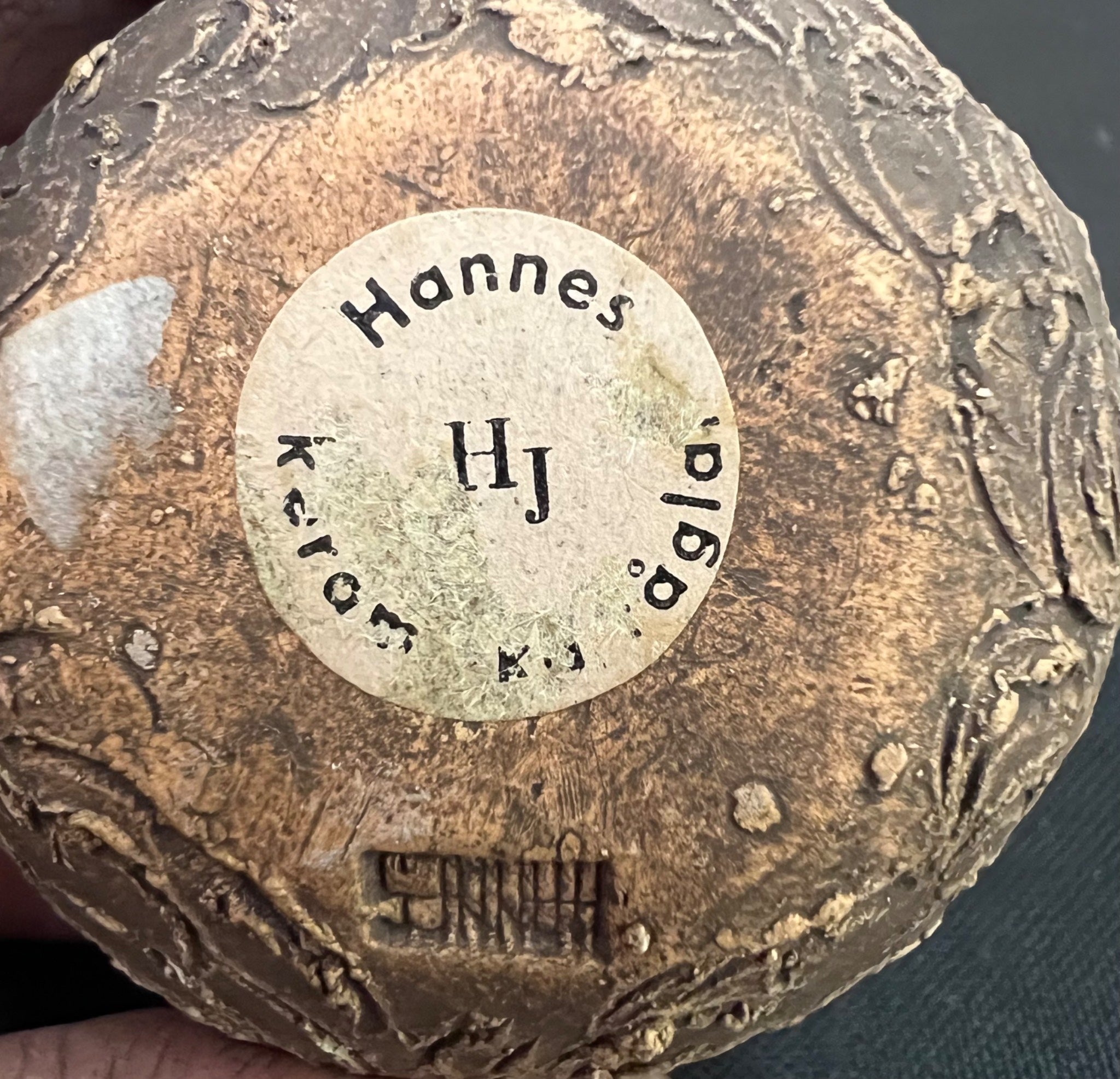 Close-up of a textured object with 'Hannes' and 'HJ' engraved on it.