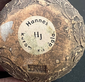 Close-up of a textured object with 'Hannes' and 'HJ' engraved on it.