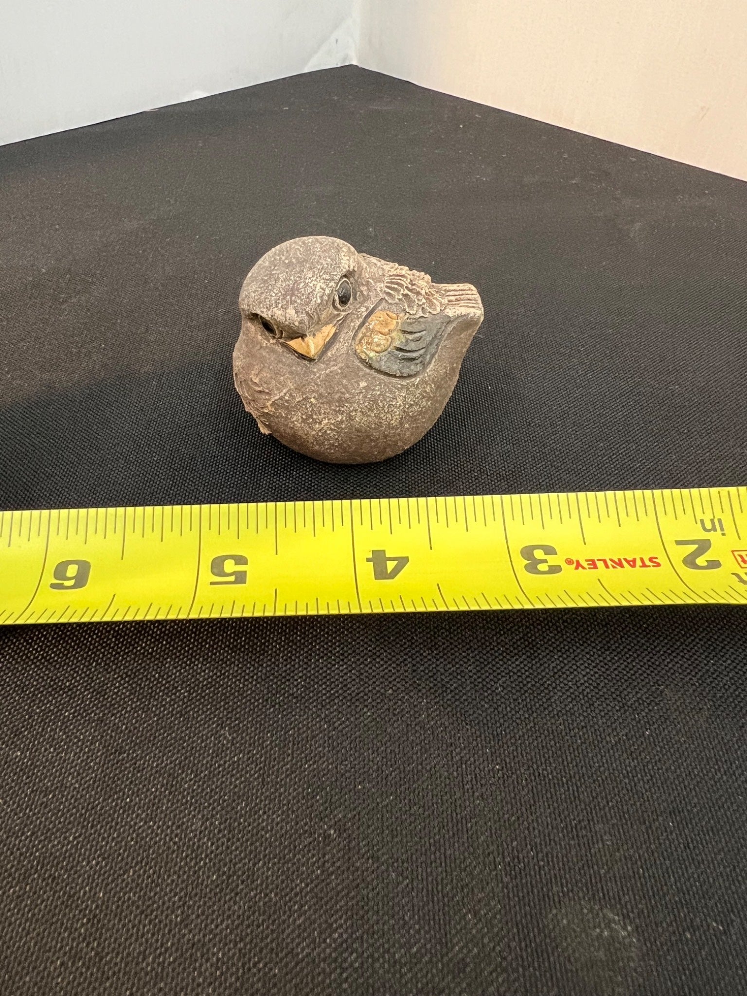 Stone sculpture of a bird with a measuring tape for scale on a black surface