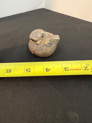 Stone sculpture of a bird with a measuring tape for scale on a black surface