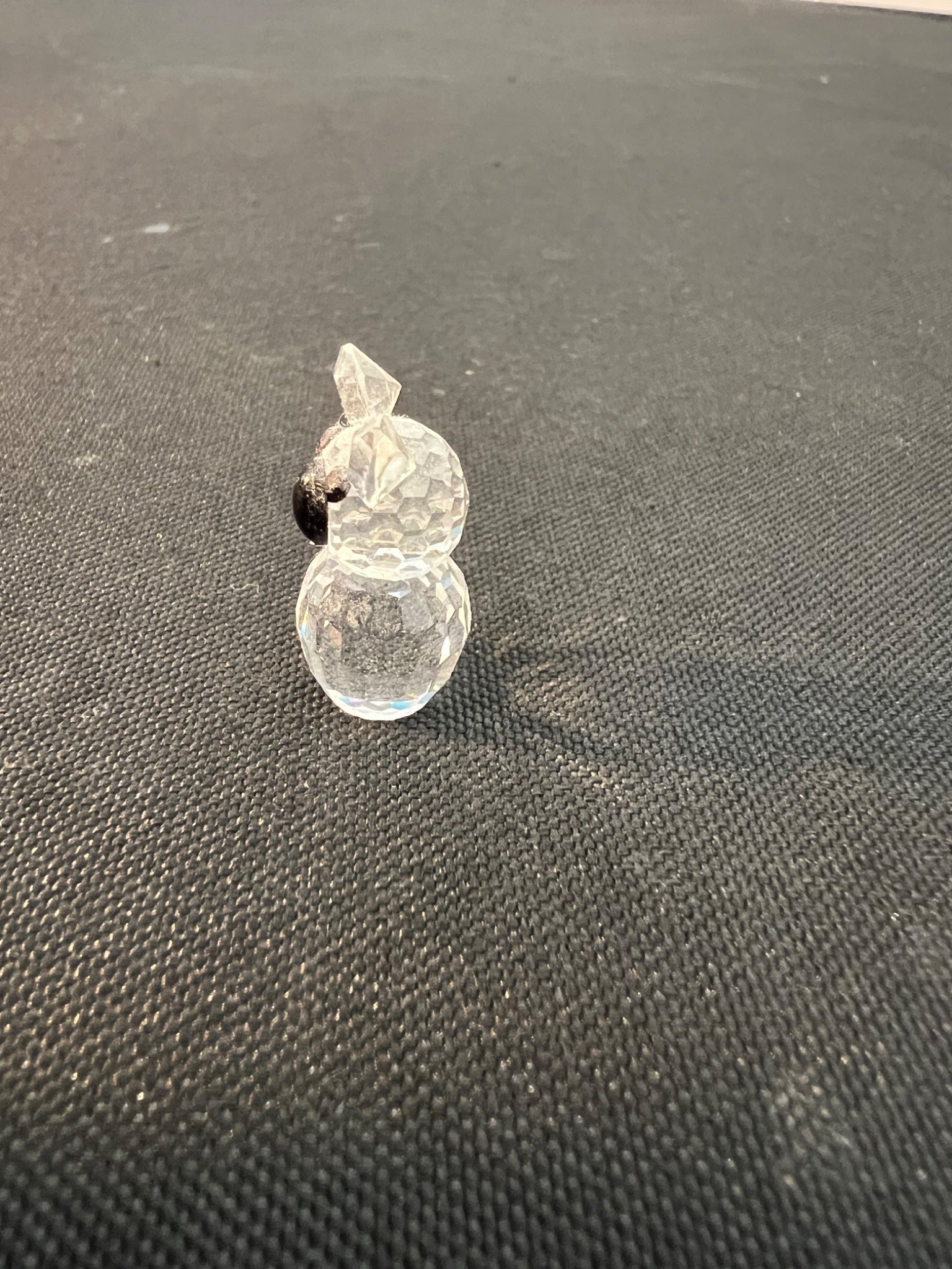 Clear glass snowman ornament on a dark textured surface