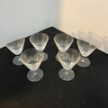 Set of six clear glass dessert cups on a dark surface with a white wall background