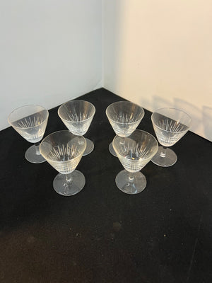 Set of six clear glass dessert cups on a dark surface with a white wall background
