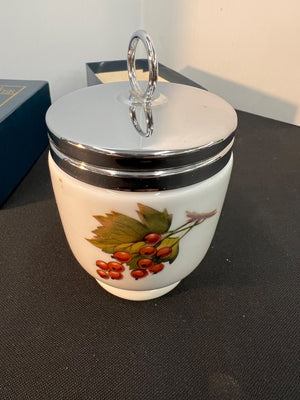 Decorative ceramic jar with a silver lid on a dark surface