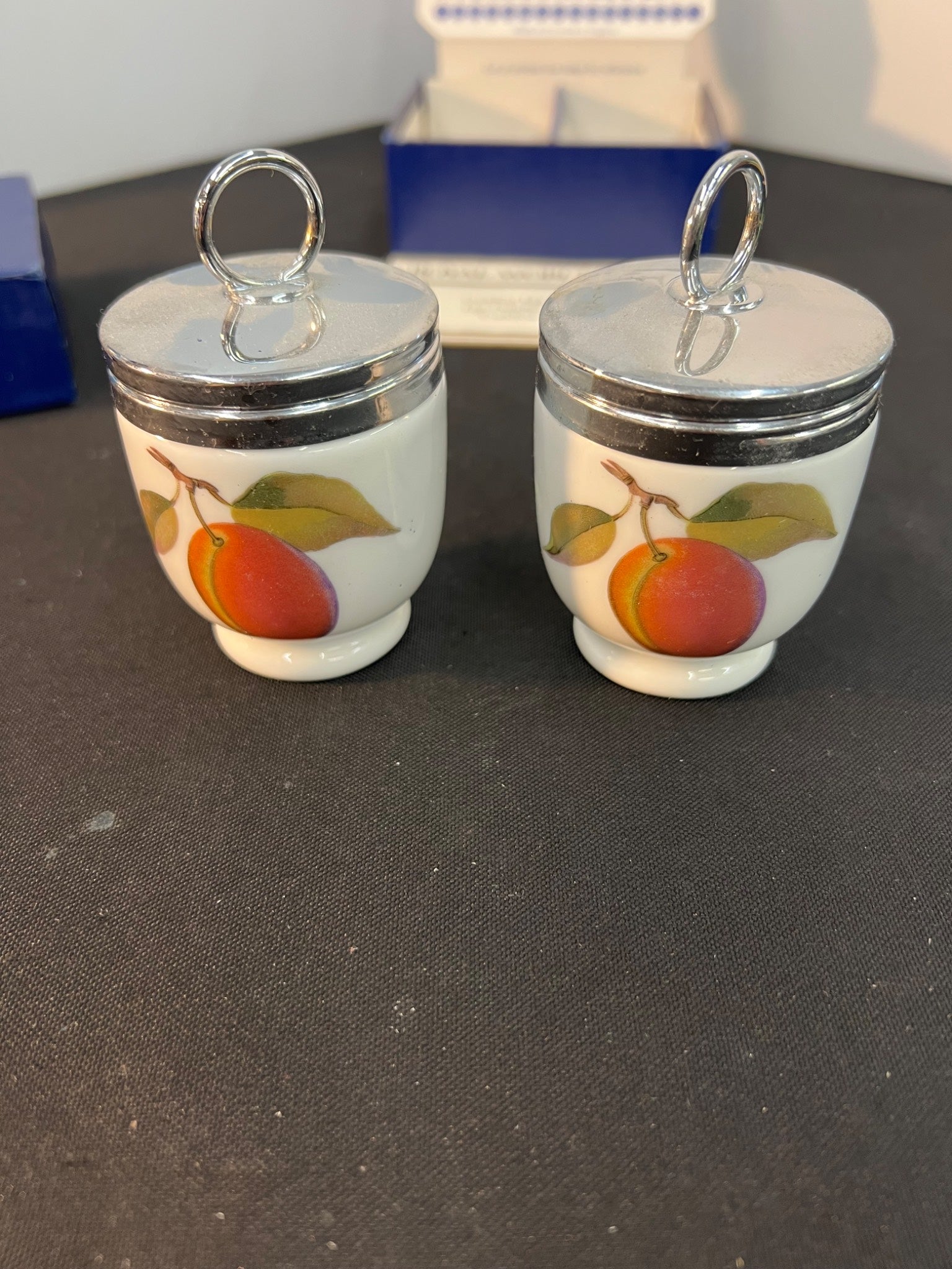 Two small ceramic jars with peach designs on a dark surface