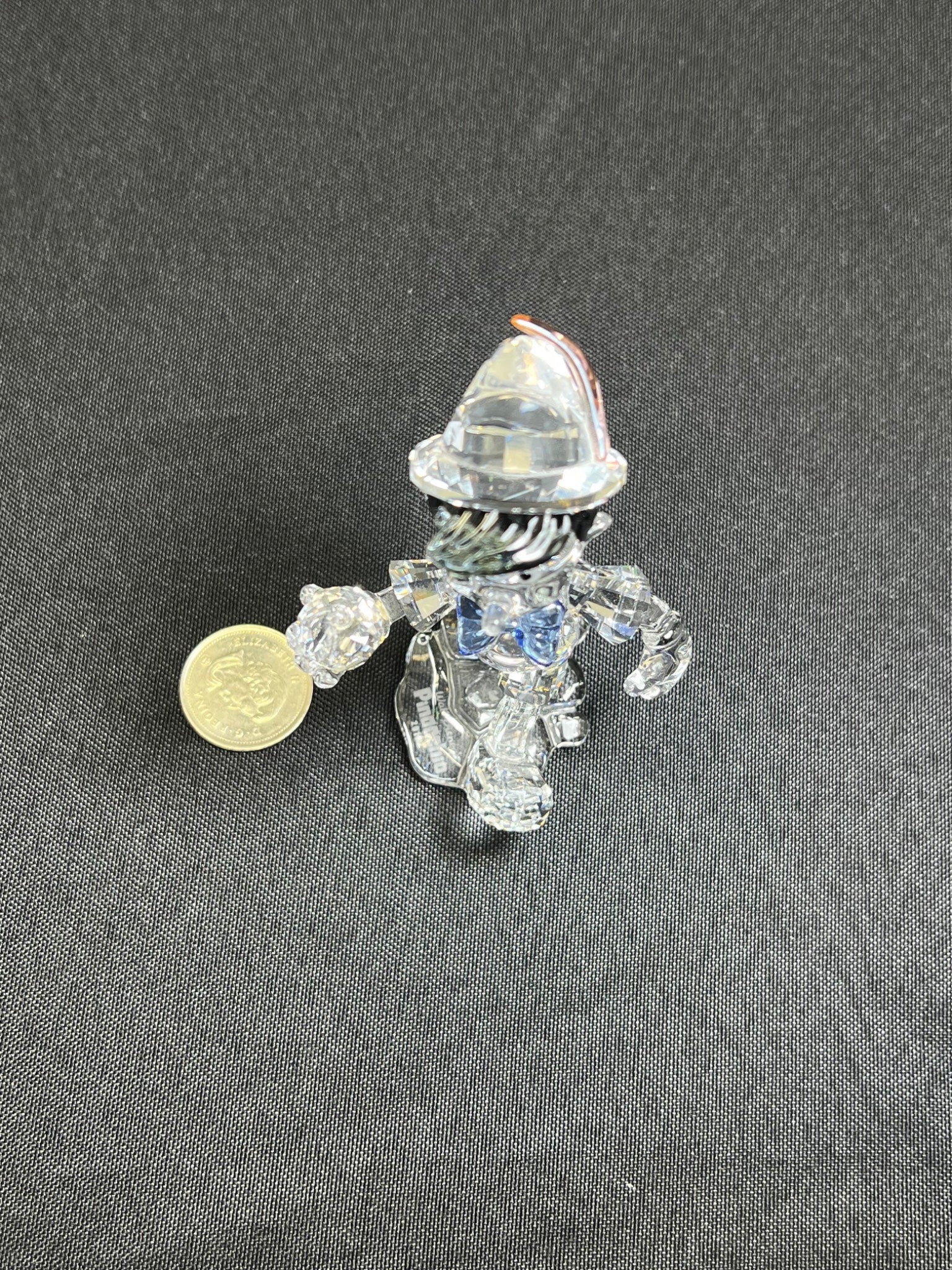 Small transparent figurine with a coin for scale on a gray background
